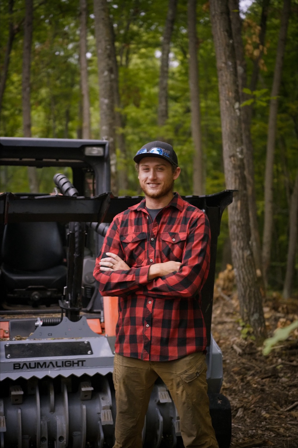 Ryan Gynnild, owner of Ryno Land Solutions, standing in front of his Baumalight forestry mulcher in the woods